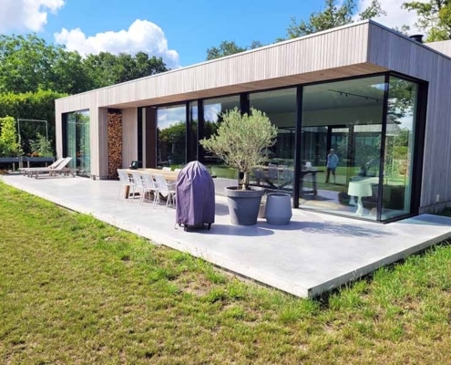 Gevlinderd betonterras met naadloze overgang naar moderne bungalow met grote glazen puien in Best